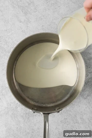 A person pouring heavy cream into a saucepan to begin making mascarpone.