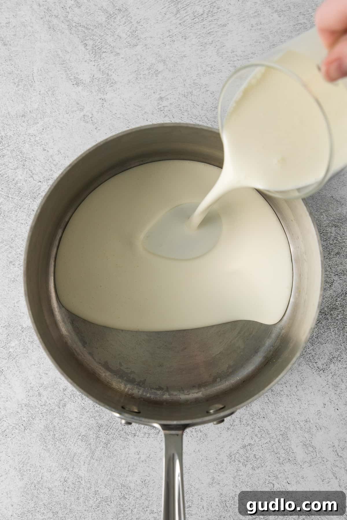 Heavy cream being carefully poured into a large, heavy-bottomed saucepan, ready for heating.