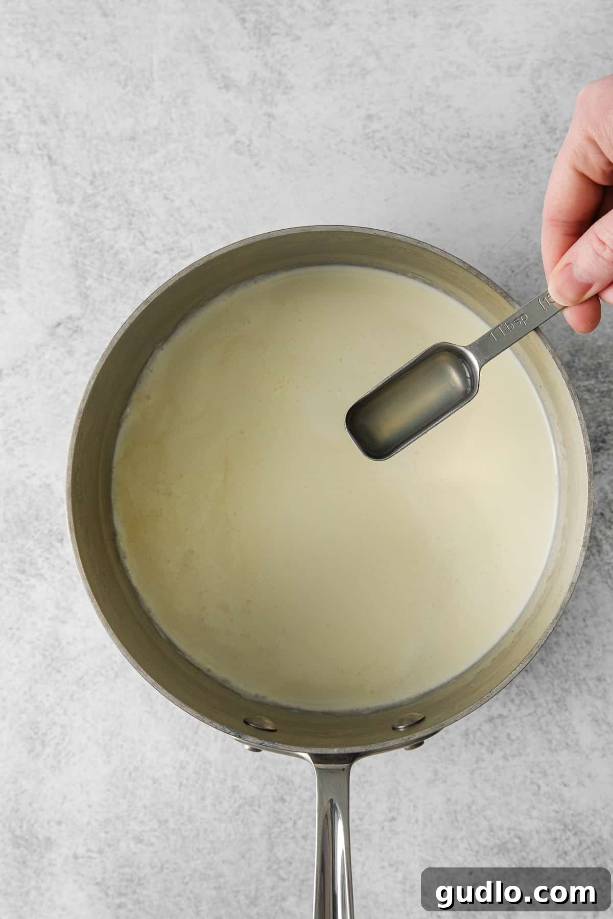 Fresh lemon juice being poured into simmering heavy cream in a saucepan, initiating the cheesemaking process.