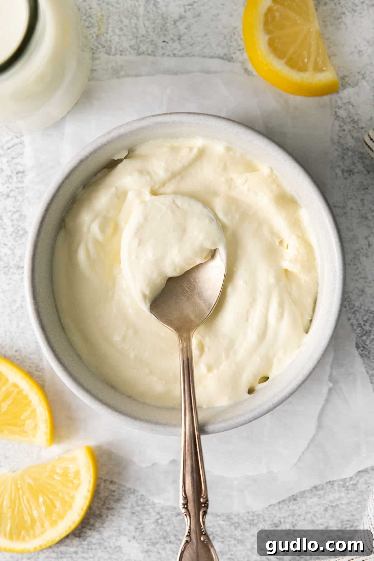 A spoon scooping creamy homemade mascarpone cheese from a small ceramic bowl, showcasing its smooth texture.