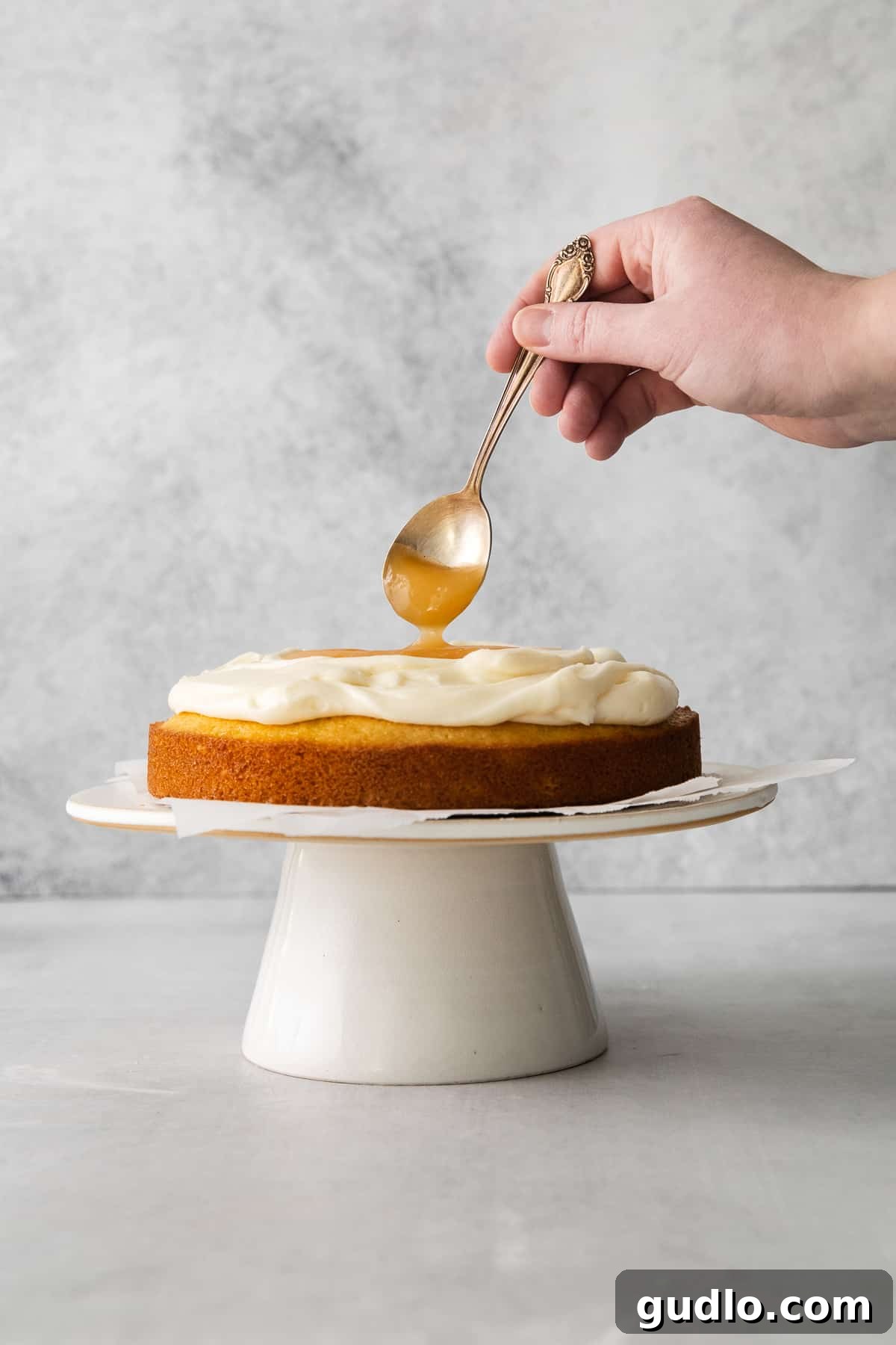 Lemon Curd Layer for Limoncello Cake Lemon curd being artfully spooned on top of a frosted layer of limoncello mascarpone cake, adding a vibrant touch.