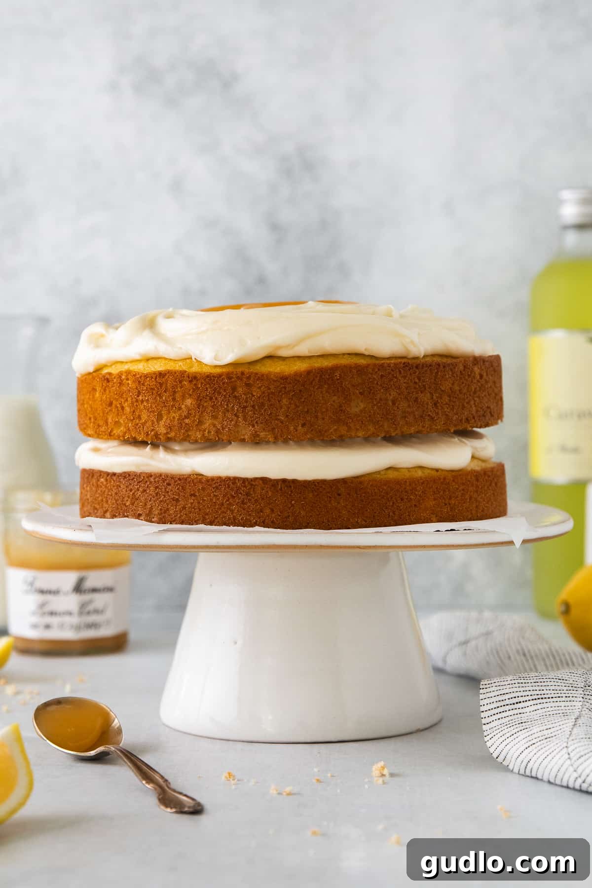 Finished Limoncello Mascarpone Cake A beautifully frosted two-layer limoncello mascarpone cake on an elegant cake plate, adorned with lemon slices.