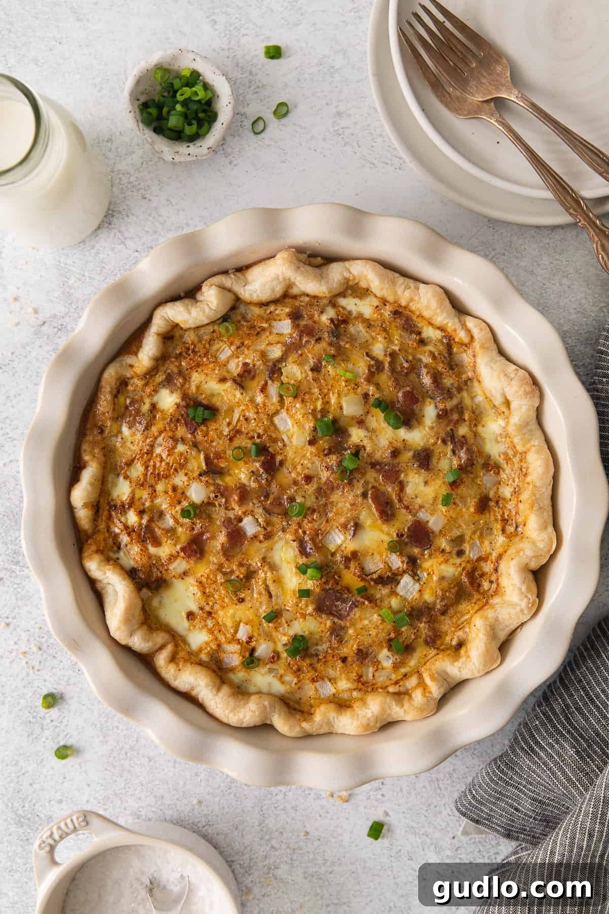 Our easy Quiche Lorraine recipe is the perfect dish for your next brunch! Made with a deliciously flakey homemade crust and filled with fluffy eggs, cheese, bacon and onions. A perfectly baked Quiche Lorraine in a rustic pie plate, golden brown and ready to be served.