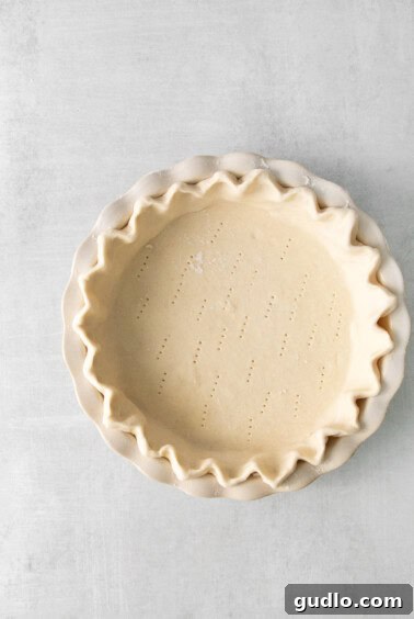 Classic French Quiche Lorraine 4 A pie crust is shown in a pie pan on a white background, with fork marks.