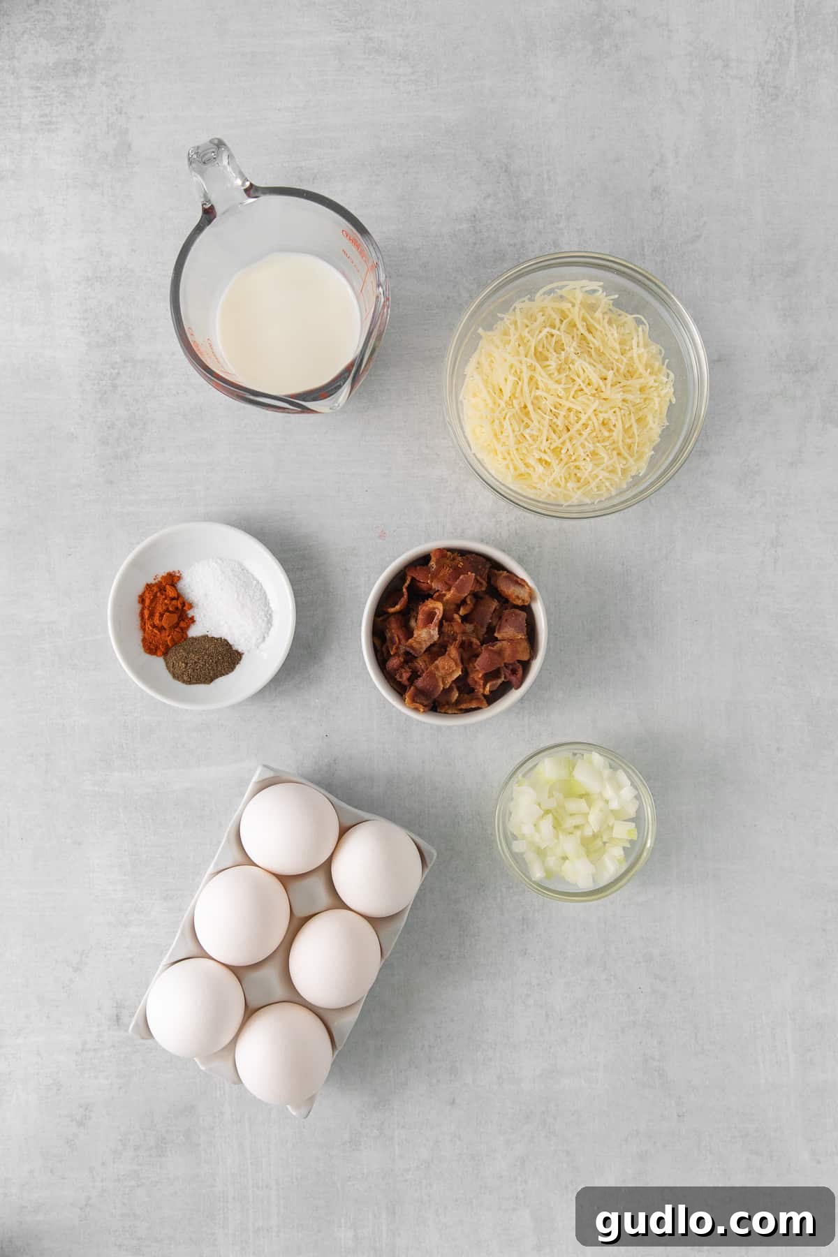 Our easy Quiche Lorraine recipe is the perfect dish for your next brunch! Made with a deliciously flakey homemade crust and filled with fluffy eggs, cheese, bacon and onions. Fresh ingredients laid out for Quiche Lorraine filling, including eggs, bacon, cheese, and onion.