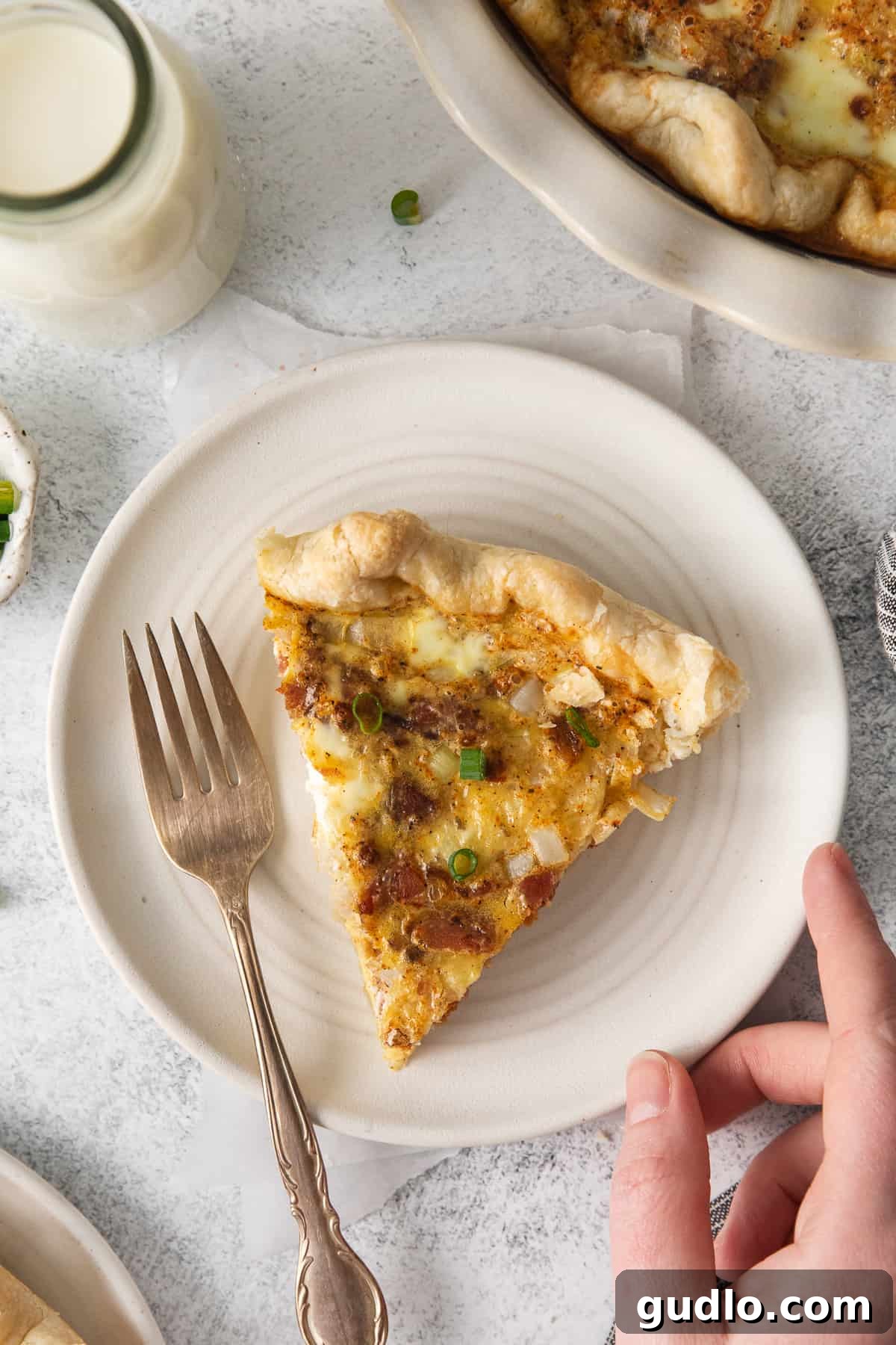 Our easy Quiche Lorraine recipe is the perfect dish for your next brunch! Made with fluffy eggs, cheese, bacon and onions. A perfect slice of Quiche Lorraine served on a white plate, showcasing its flaky crust and rich filling.