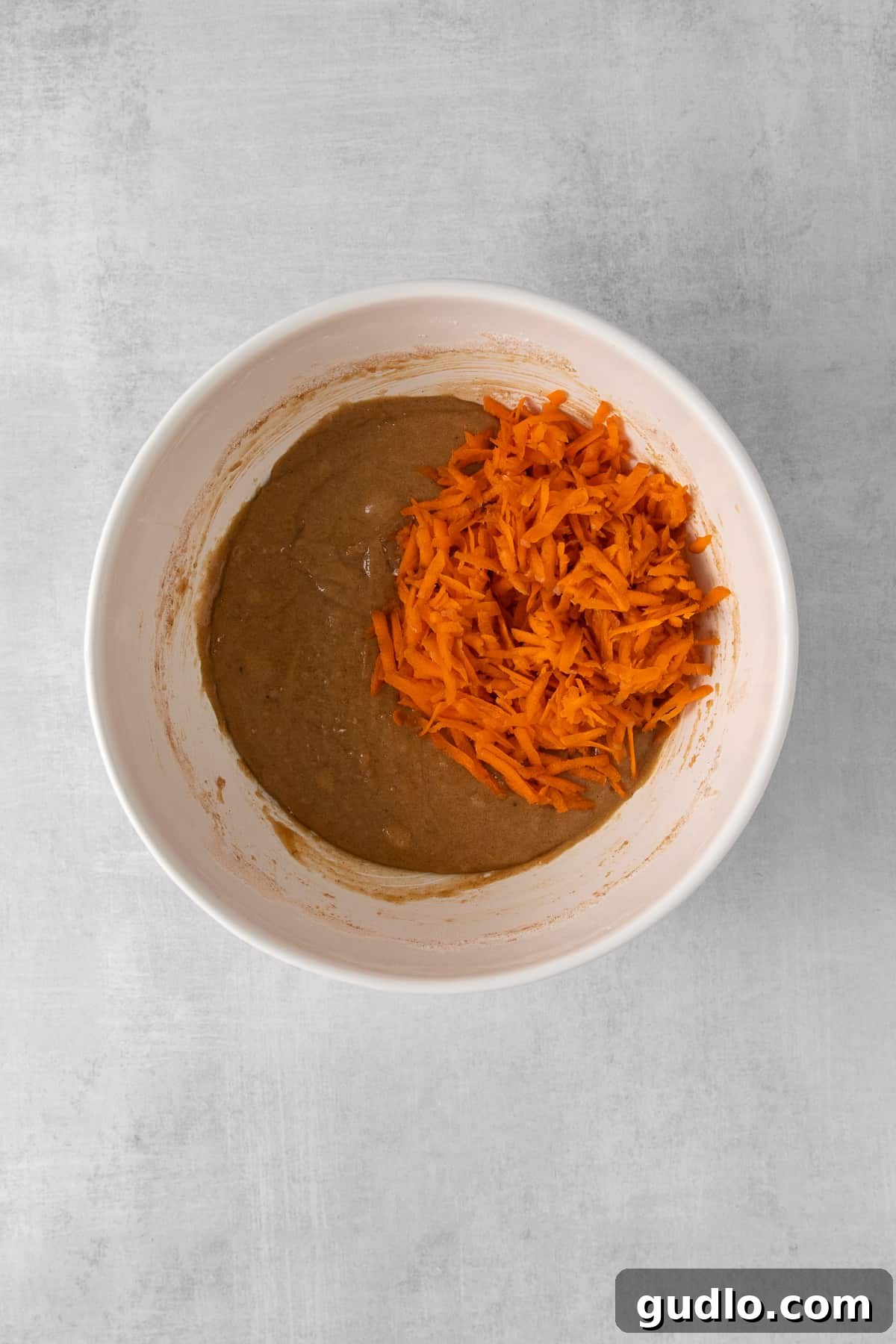 Close-up shot of golden-orange carrot cake batter in a large mixing bowl, showcasing the flecks of shredded carrots and spices.