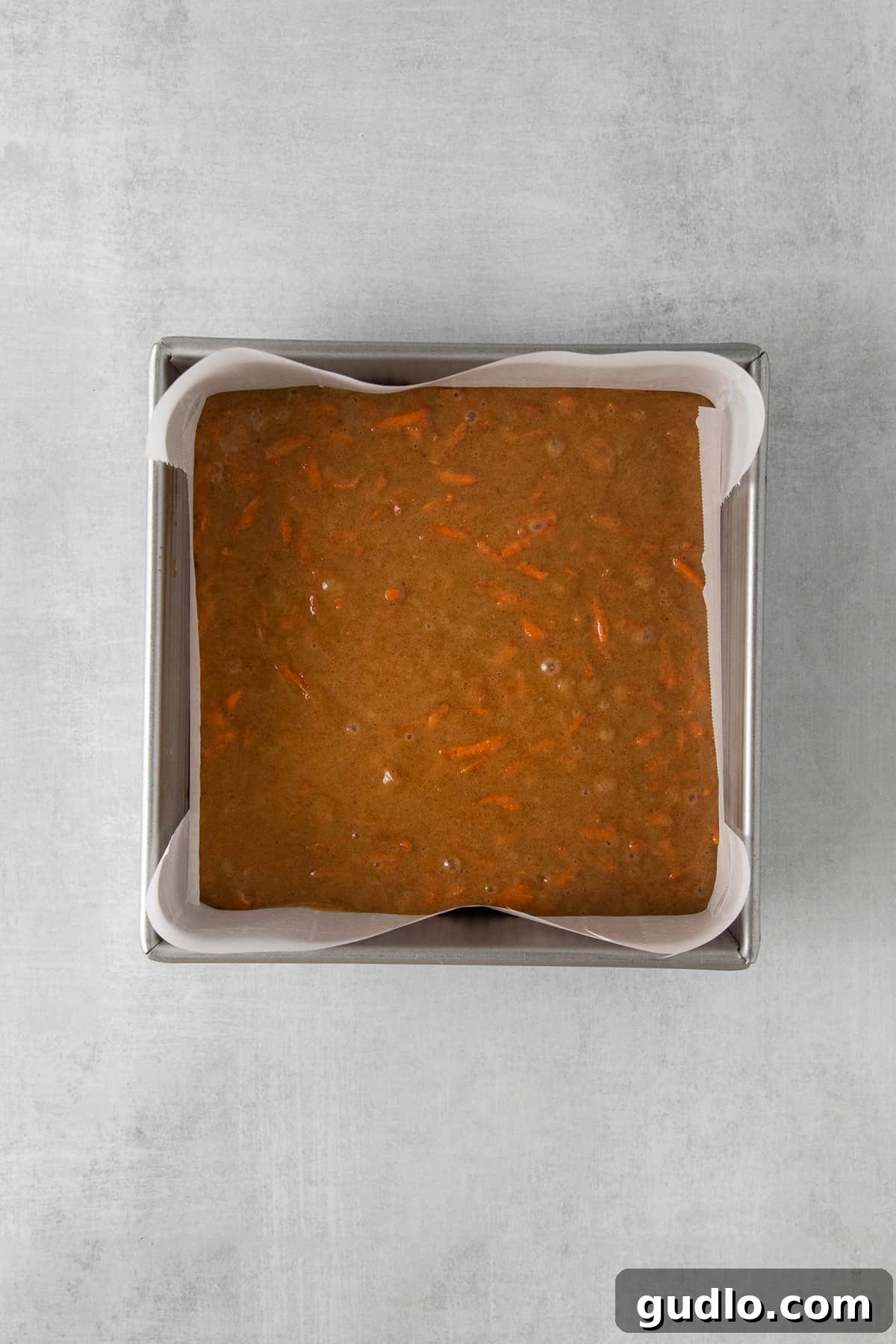 Carrot cake batter evenly spread in a square glass baking dish, ready to be placed in the oven.