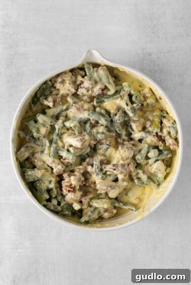 A white mixing bowl containing the ricotta, egg, asparagus, and Italian sausage filling mixture.