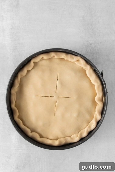 An unbaked Italian Easter pie in a springform pan with the top crust sealed and slits cut.