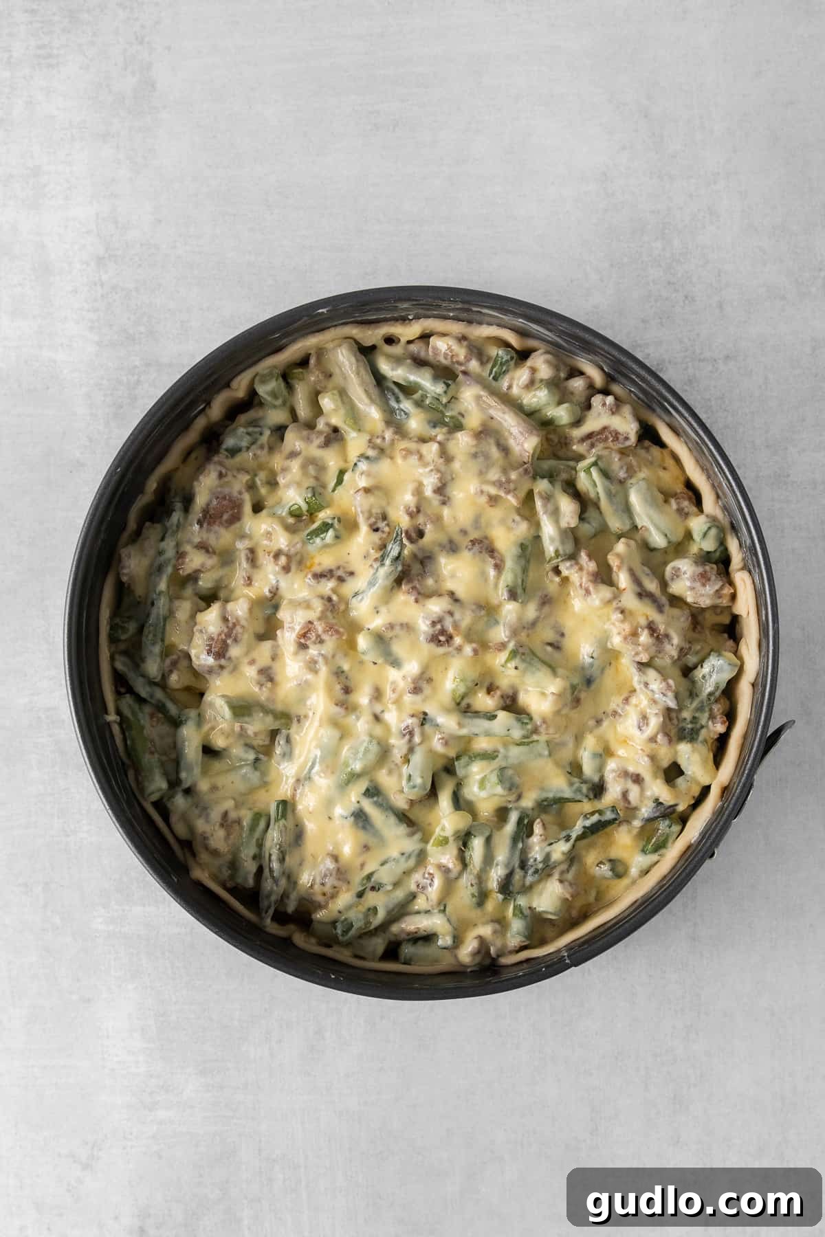 The rich and creamy Italian Easter pie filling being added to a springform pan lined with crust and meat.