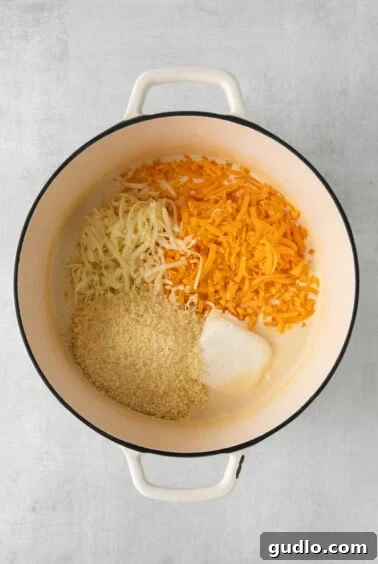 Four varieties of cheese melting into a creamy sauce in a stock pot.