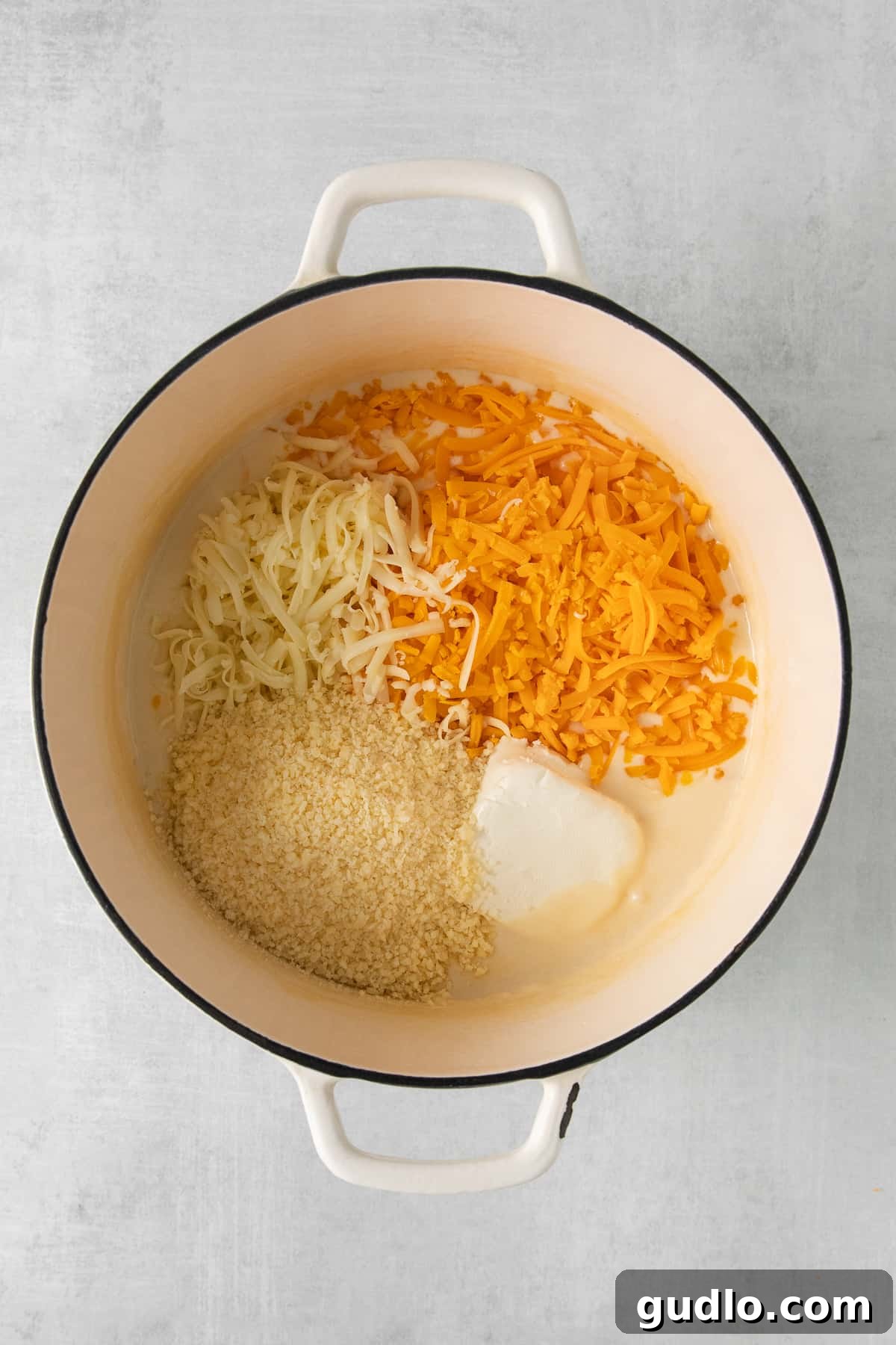 Four varieties of cheese melting together in a large stock pot, forming a smooth, creamy sauce.