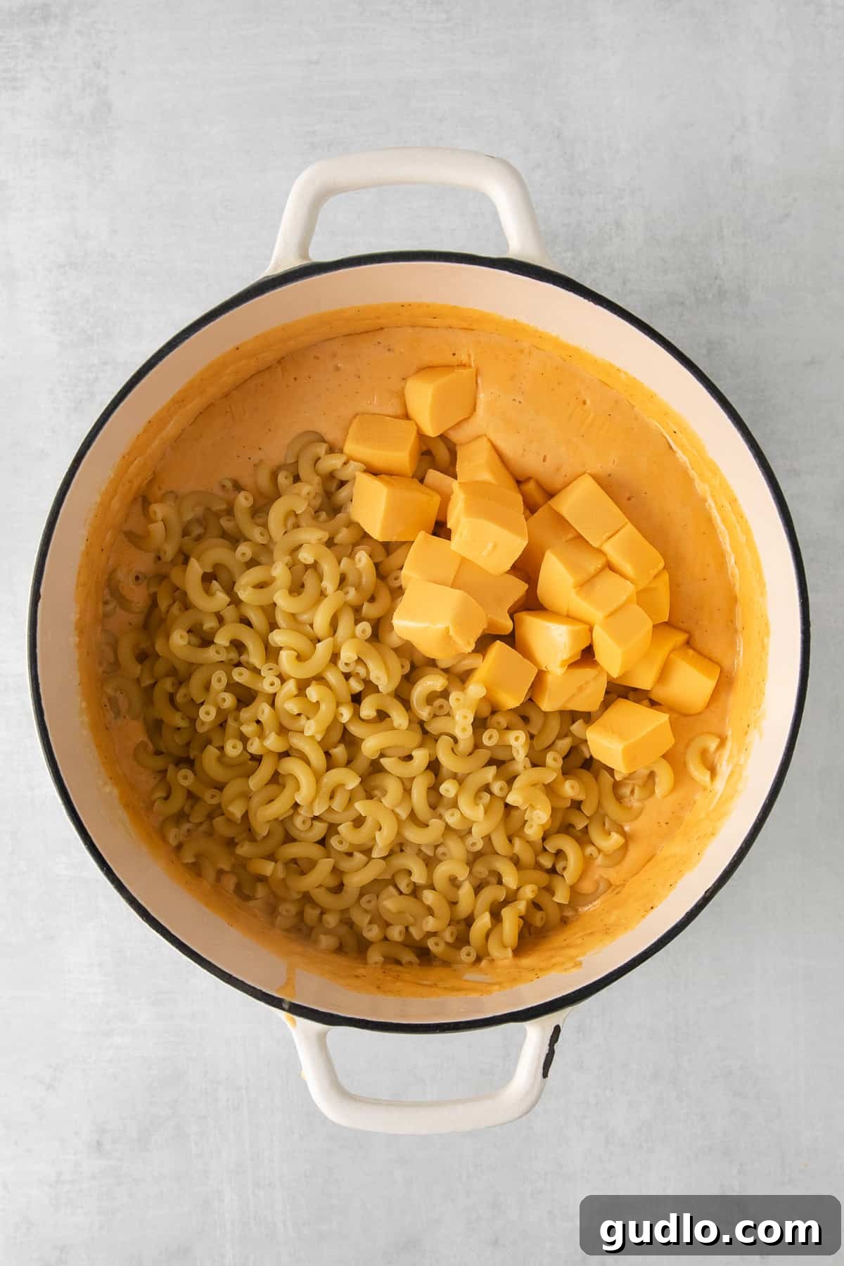 Cooked elbow pasta mixed with chunks of Velveeta cheese in a large stock pot, waiting for the cheese sauce.
