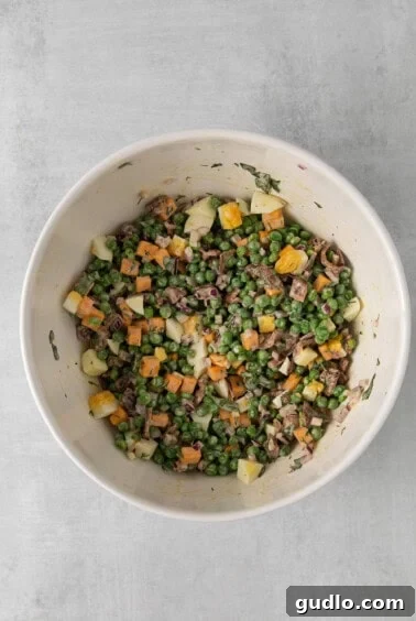 Creamy English Pea Salad 11 English pea salad tossed in creamy dressing with eggs, in a bowl.