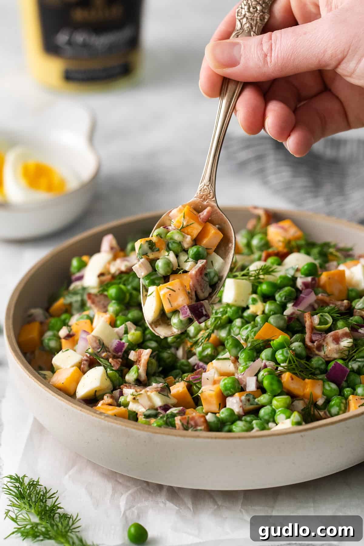 Creamy English Pea Salad 7 A spoonful of creamy English pea salad, highlighting the texture and mixture of peas, cheese, and bacon, ready to be tasted.