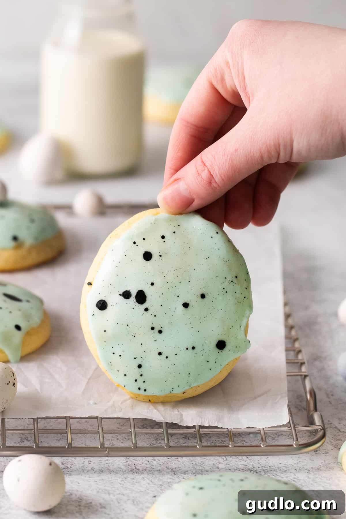 A hand holding a perfectly glazed lemon ricotta cookie with sprinkles, with a bite taken out.