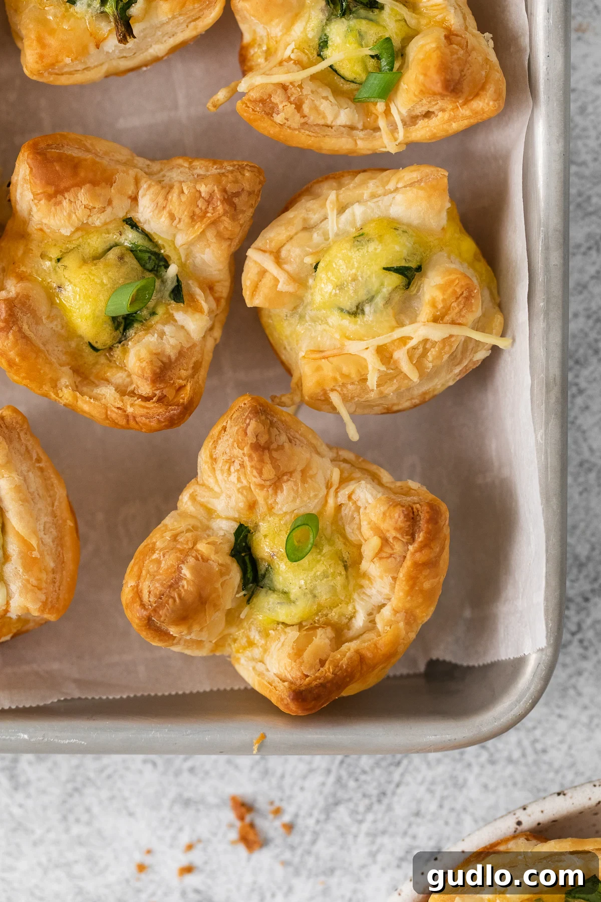 This mini quiche florentine offers savory, cheesy goodness with every bite! Enjoy a tasty blend of spinach, gruyere cheese, and creamy egg filling enveloped in a flaky pie crust that will take you to breakfast heaven. Mini quiche florentine on a baking tray.