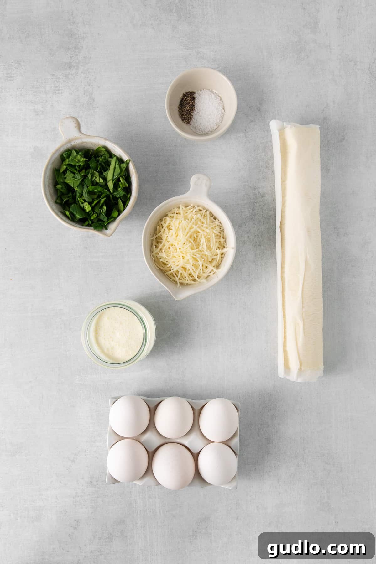 This mini quiche florentine offers savory, cheesy goodness with every bite! Enjoy a tasty blend of spinach, gruyere cheese, and creamy egg filling enveloped in a flaky pie crust that will take you to breakfast heaven. Ingredients for quiche florentine in bowls.
