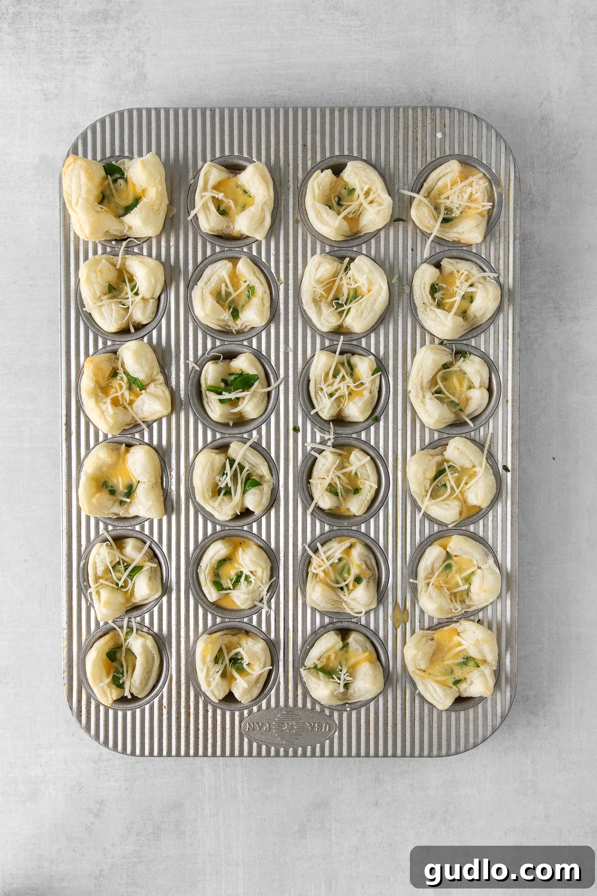 This mini quiche florentine offers savory, cheesy goodness with every bite! Enjoy a tasty blend of spinach, gruyere cheese, and creamy egg filling enveloped in a flaky pie crust that will take you to breakfast heaven. Mini quiche florentine in a muffin tin.