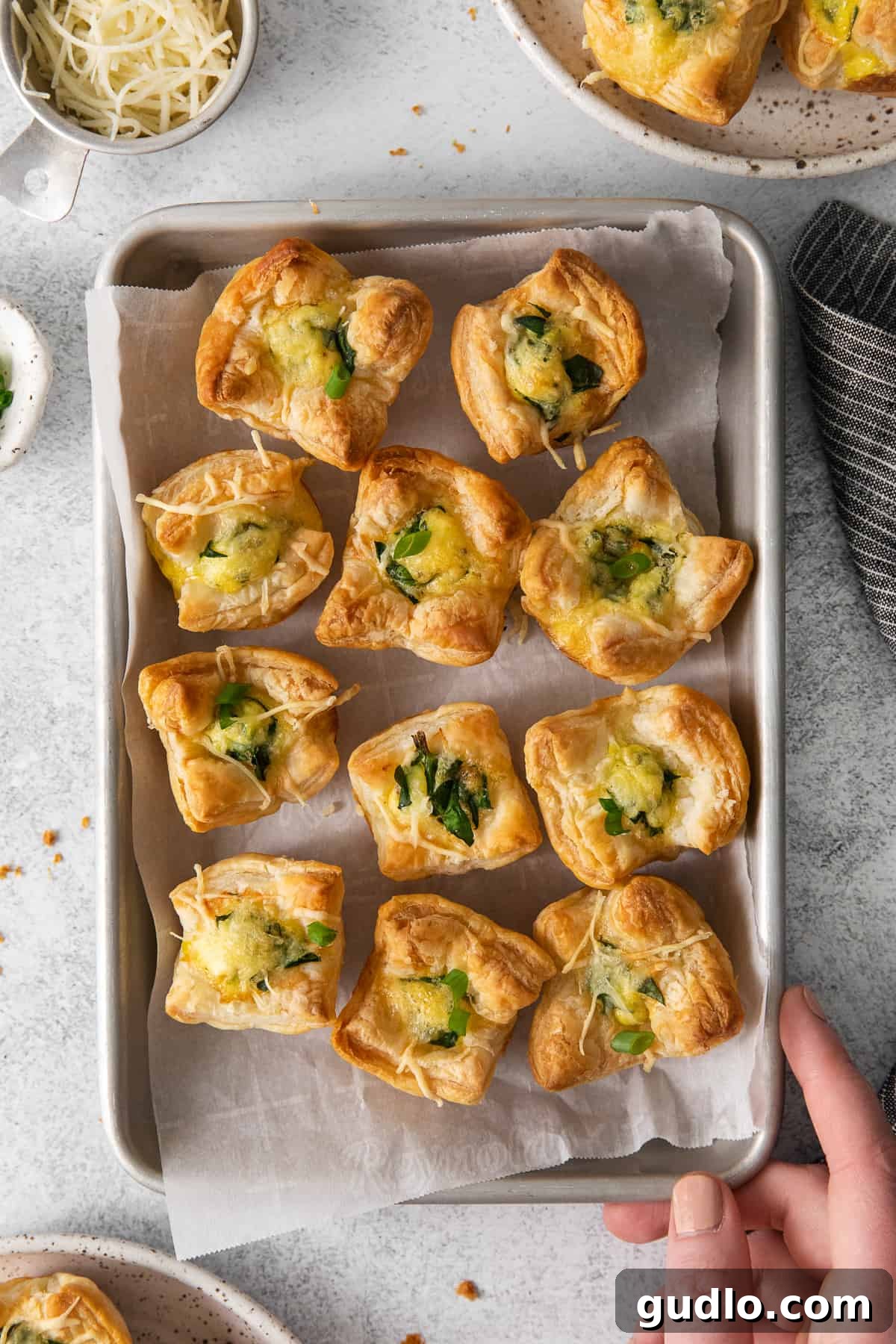 This mini quiche florentine offers savory, cheesy goodness with every bite! Enjoy a tasty blend of spinach, gruyere cheese, and creamy egg filling enveloped in a flaky pie crust that will take you to breakfast heaven. Mini quiche florentines on a baking tray with parchment paper.