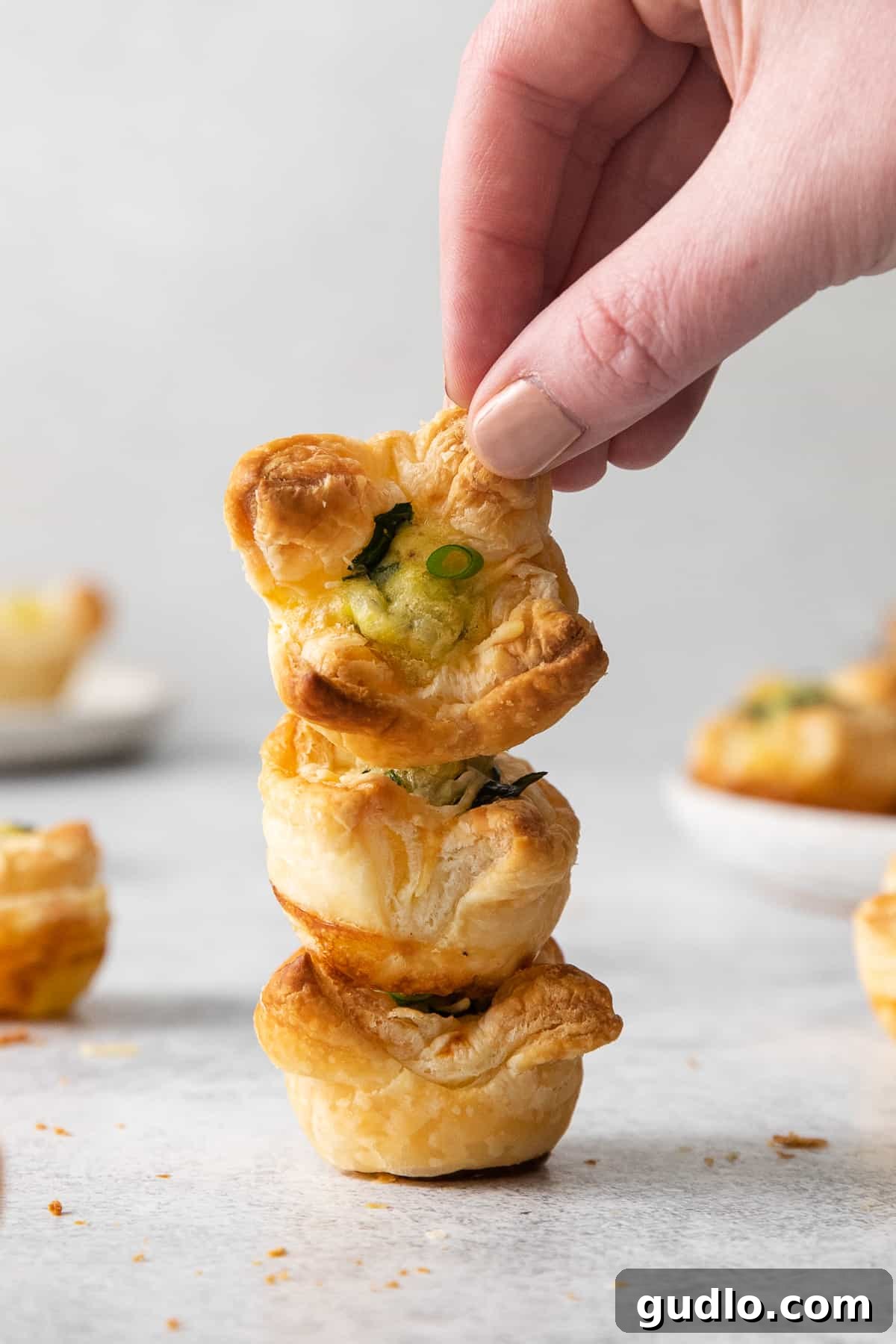 This mini quiche florentine offers savory, cheesy goodness with every bite! Enjoy a tasty blend of spinach, gruyere cheese, and creamy egg filling enveloped in a flaky pie crust that will take you to breakfast heaven. Mini quiche florentine stacked 4 high on a plate.
