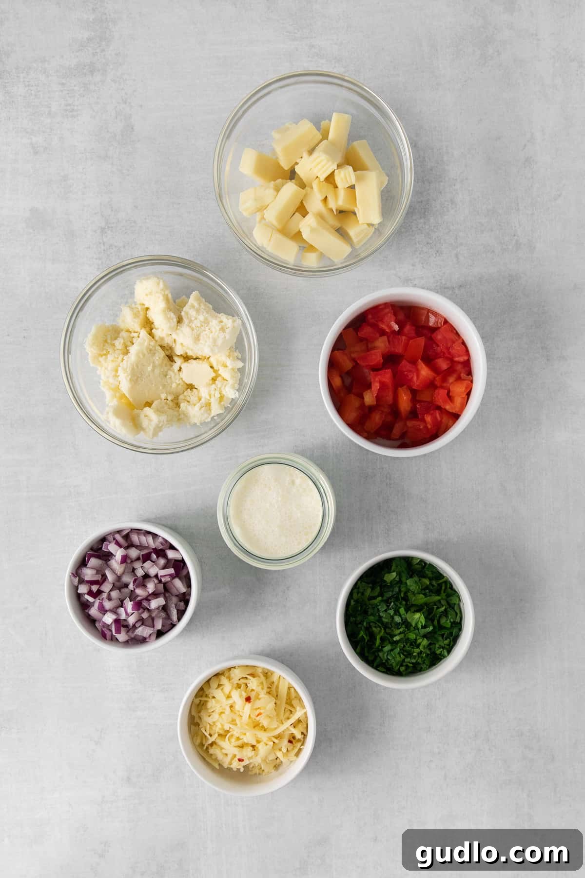 Bowls of diced American cheese, shredded pepper jack, crumbled Cotija cheese, minced cilantro, diced tomatoes, and red onion, representing the fresh ingredients for Cotija queso dip.