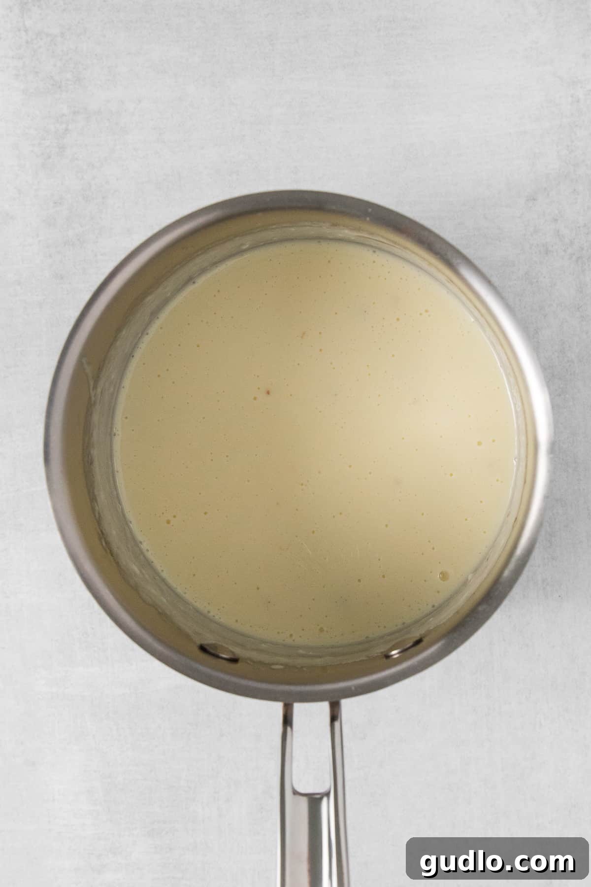 Cotija queso dip being stirred in a saucepan over low heat, showcasing its creamy texture before garnishing.