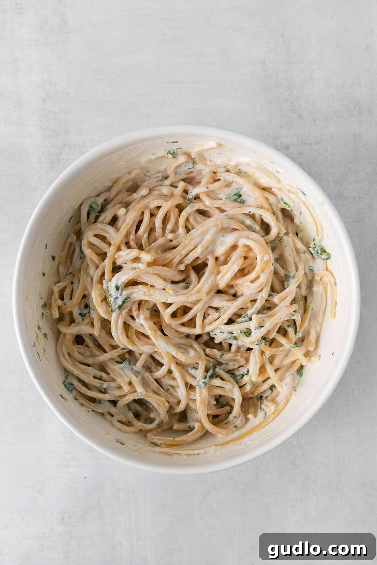 A bowl of lemon ricotta pasta adorned with fresh basil and parsley.