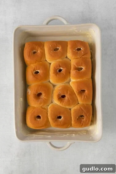 Hawaiian rolls placed in a greased baking dish with holes pushed in the center.