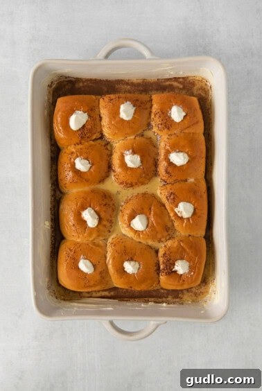Hawaiian rolls in a baking dish being stuffed with whipped cream cheese.