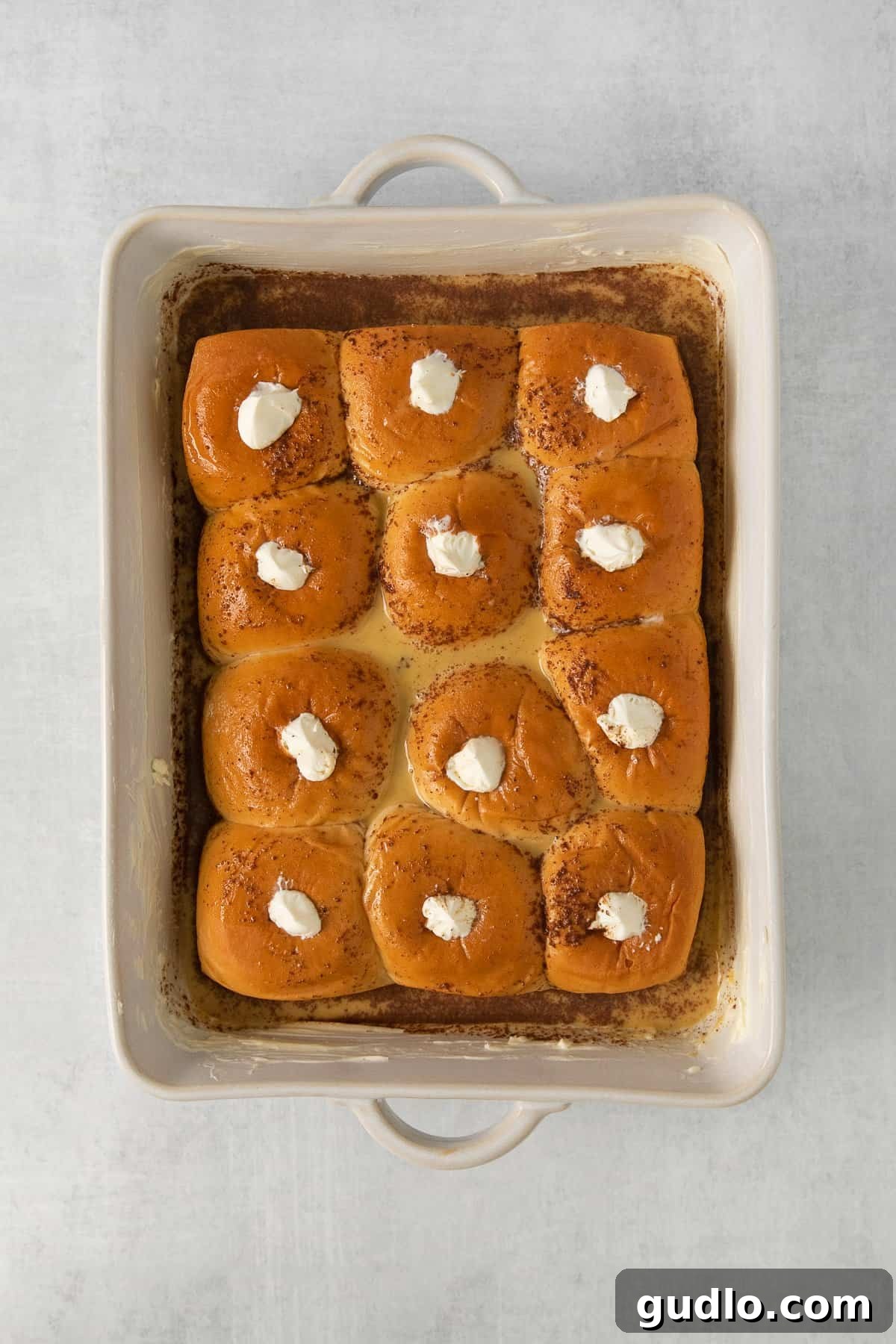 Baked Stuffed Hawaiian Roll French Toast Close-up of baked Stuffed Hawaiian Roll French Toast in a casserole dish, glistening with golden crust and hints of cream cheese.