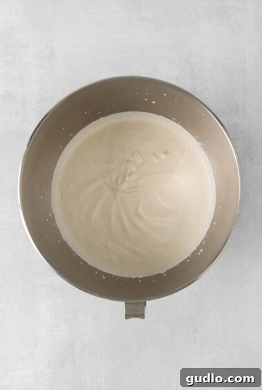Whipped cream in a metal bowl on a white background, showing soft peaks.