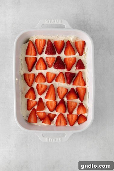 A white baking dish with strawberries layered into the tiramisu assembly.