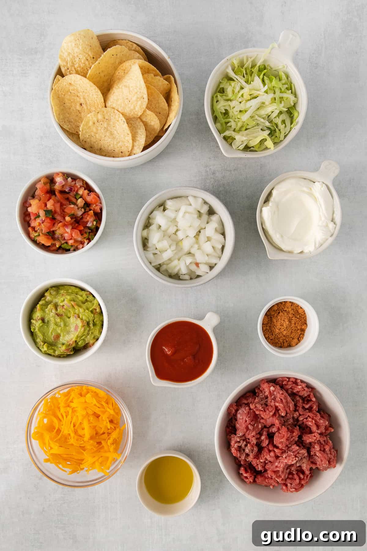 Ingredients for beef nachos in bowls, neatly arranged on a white background.