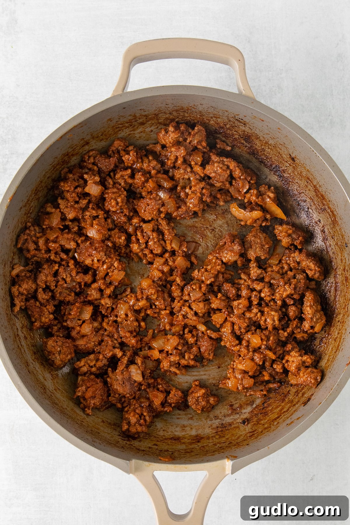 Ground beef cooking in a skillet with diced onions, ready for seasoning.