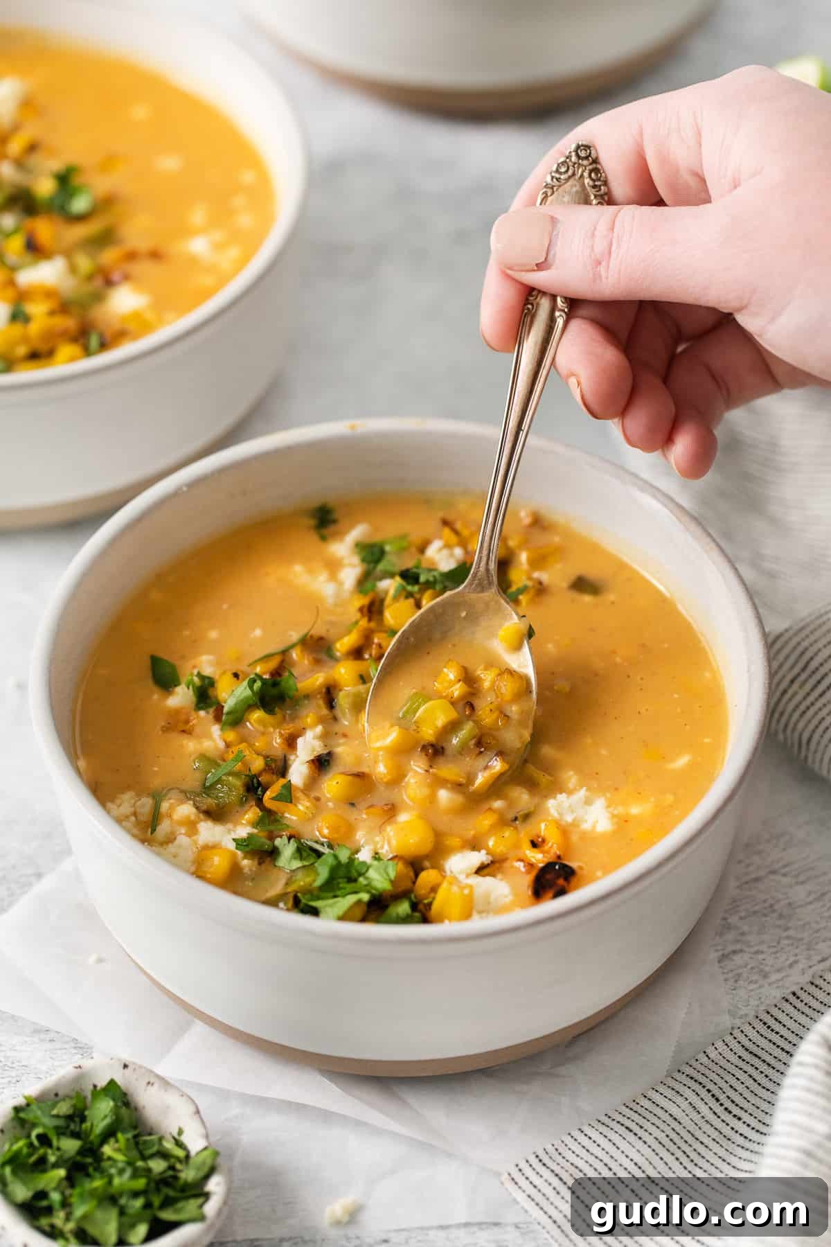 A steaming bowl of creamy Mexican Street Corn Soup, garnished with fresh cilantro and cotija cheese, ready to be enjoyed with a spoon.