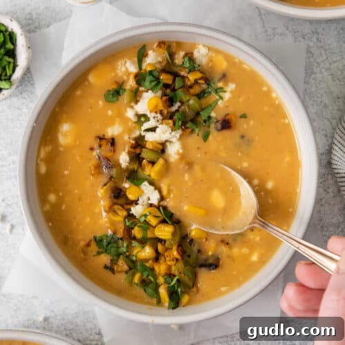 A beautifully presented bowl of creamy Mexican Street Corn Soup, garnished with charred corn, cotija cheese, cilantro, and a lime wedge.