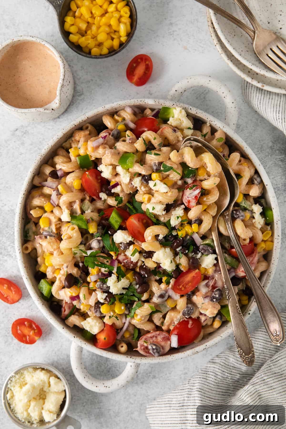 Fiesta Pasta Salad 2 A large bowl of creamy Mexican pasta salad with two serving spoons, garnished with fresh cilantro and queso fresco, ready to be enjoyed.