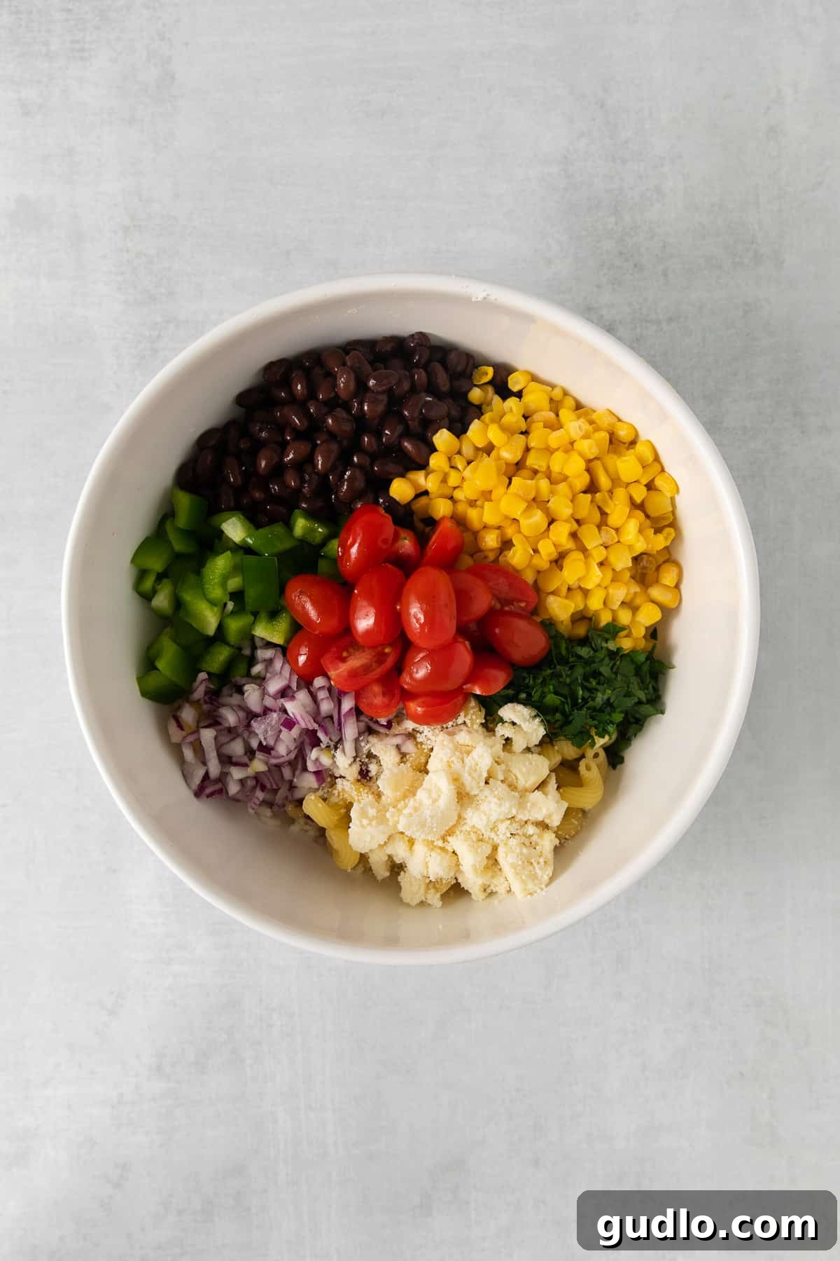 Fiesta Pasta Salad 4 Close-up of fresh ingredients for Mexican pasta salad in a large mixing bowl, showcasing black beans, corn, cherry tomatoes, bell peppers, and cilantro.