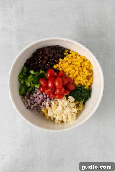 Fiesta Pasta Salad 6 A large bowl filled with various colorful ingredients for Mexican pasta salad, including pasta, black beans, corn, tomatoes, bell peppers, and cilantro, before the dressing is added.