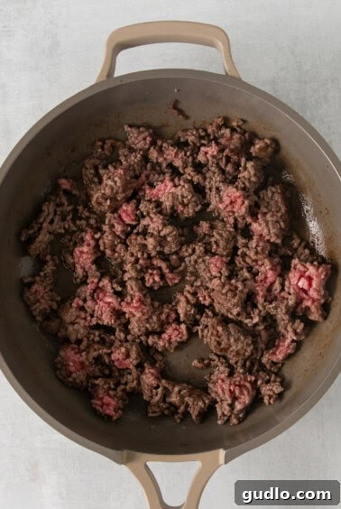 Ground beef cooking in a skillet on a white surface.