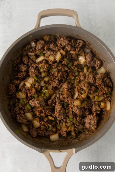 A skillet filled with seasoned ground beef, onions, and bell peppers.