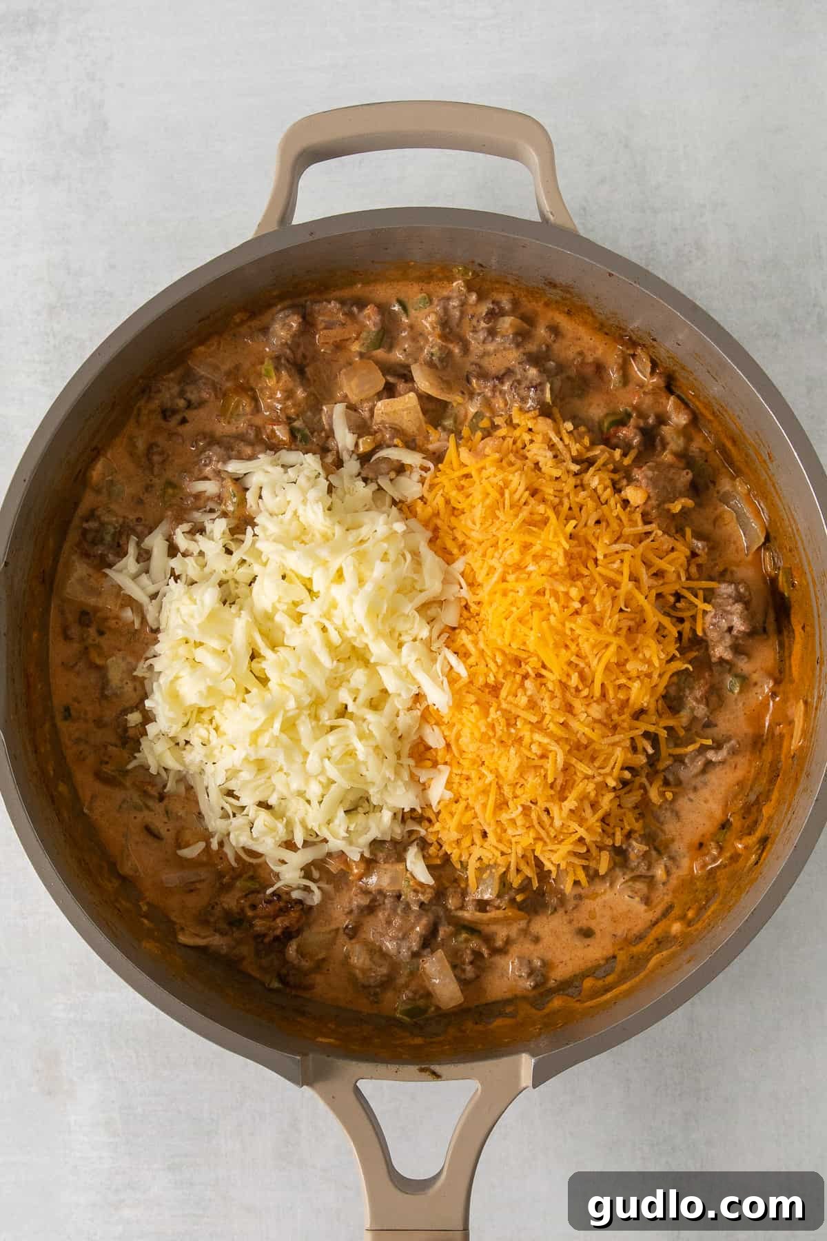 Melting Cheese Over Savory Taco Meat Perfectly seasoned taco meat topped with a generous layer of shredded cheese, melting beautifully in a hot skillet.