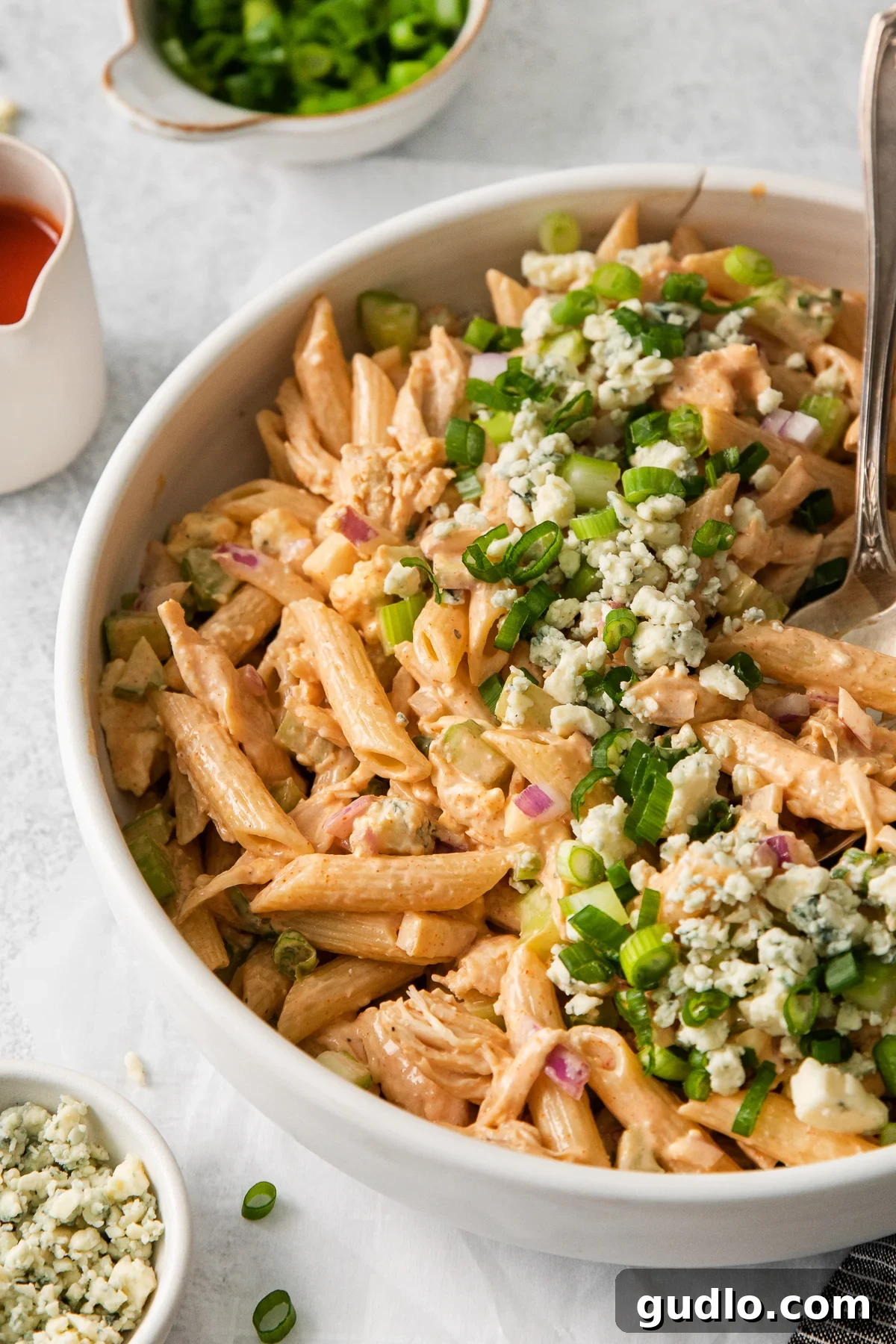 A large bowl of creamy buffalo chicken pasta salad, garnished with fresh herbs and blue cheese crumbles, ready to be served at a gathering.