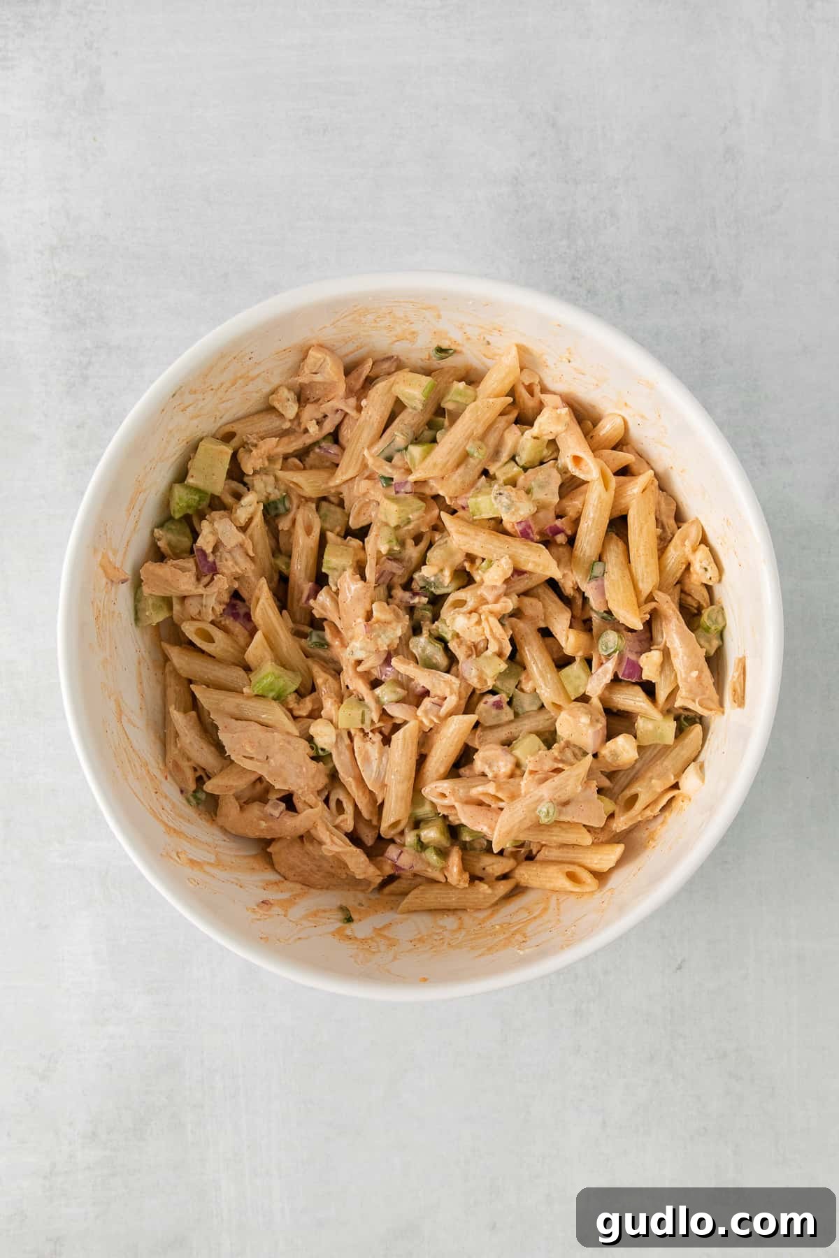 All the components of the buffalo chicken pasta salad – pasta, chicken, vegetables, and dressing – tossed together in a large mixing bowl, ensuring everything is evenly coated.