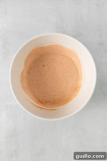 The vibrant red and creamy buffalo dressing being whisked in a mixing bowl, showcasing its smooth texture and readiness for combining with other ingredients.
