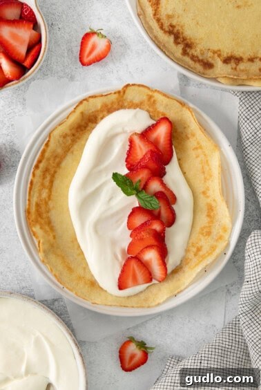 A strawberry crepe, filled and folded, on a white plate.