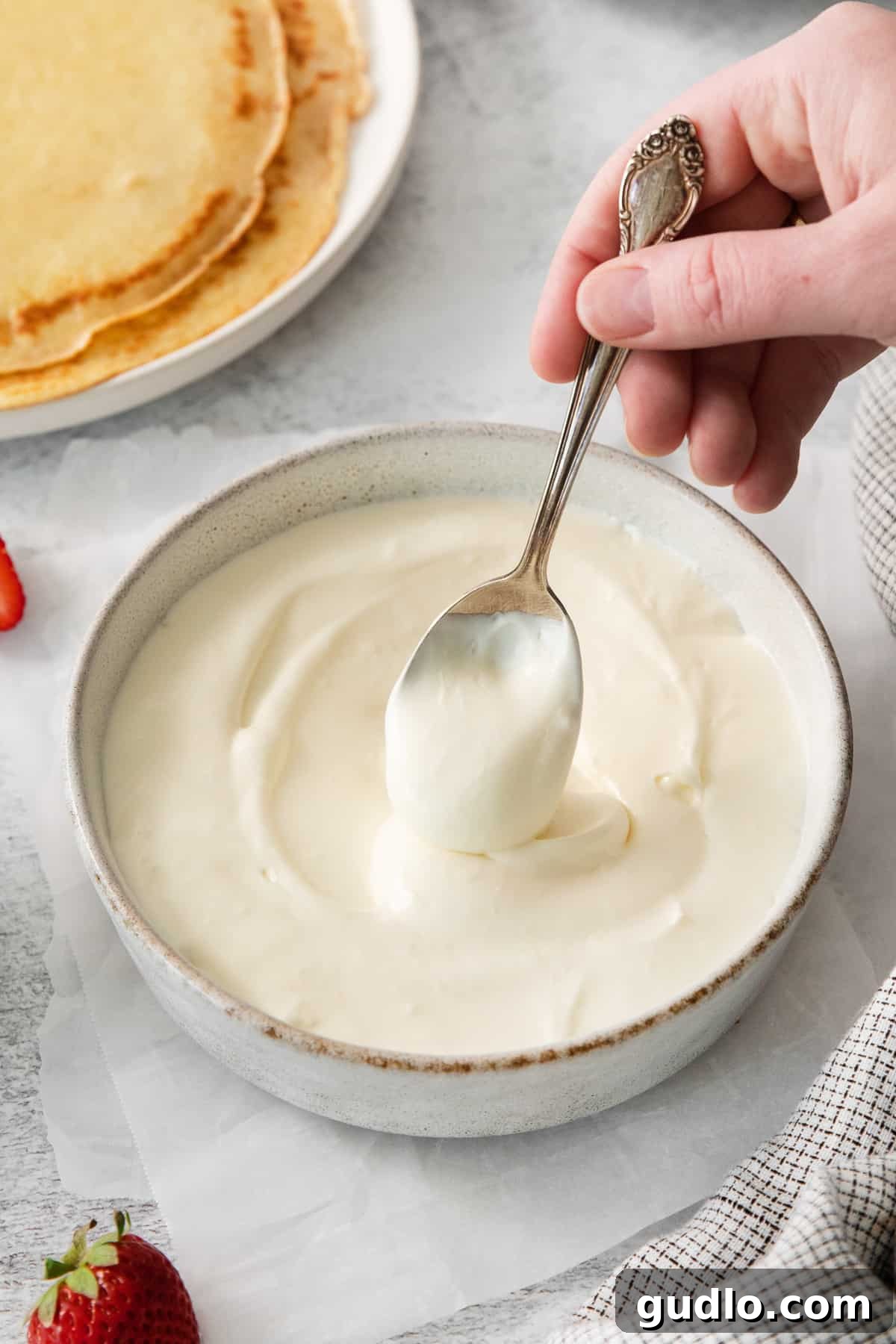 A spoon full of rich strawberry cream cheese filling, ready to be spread onto a crepe.
