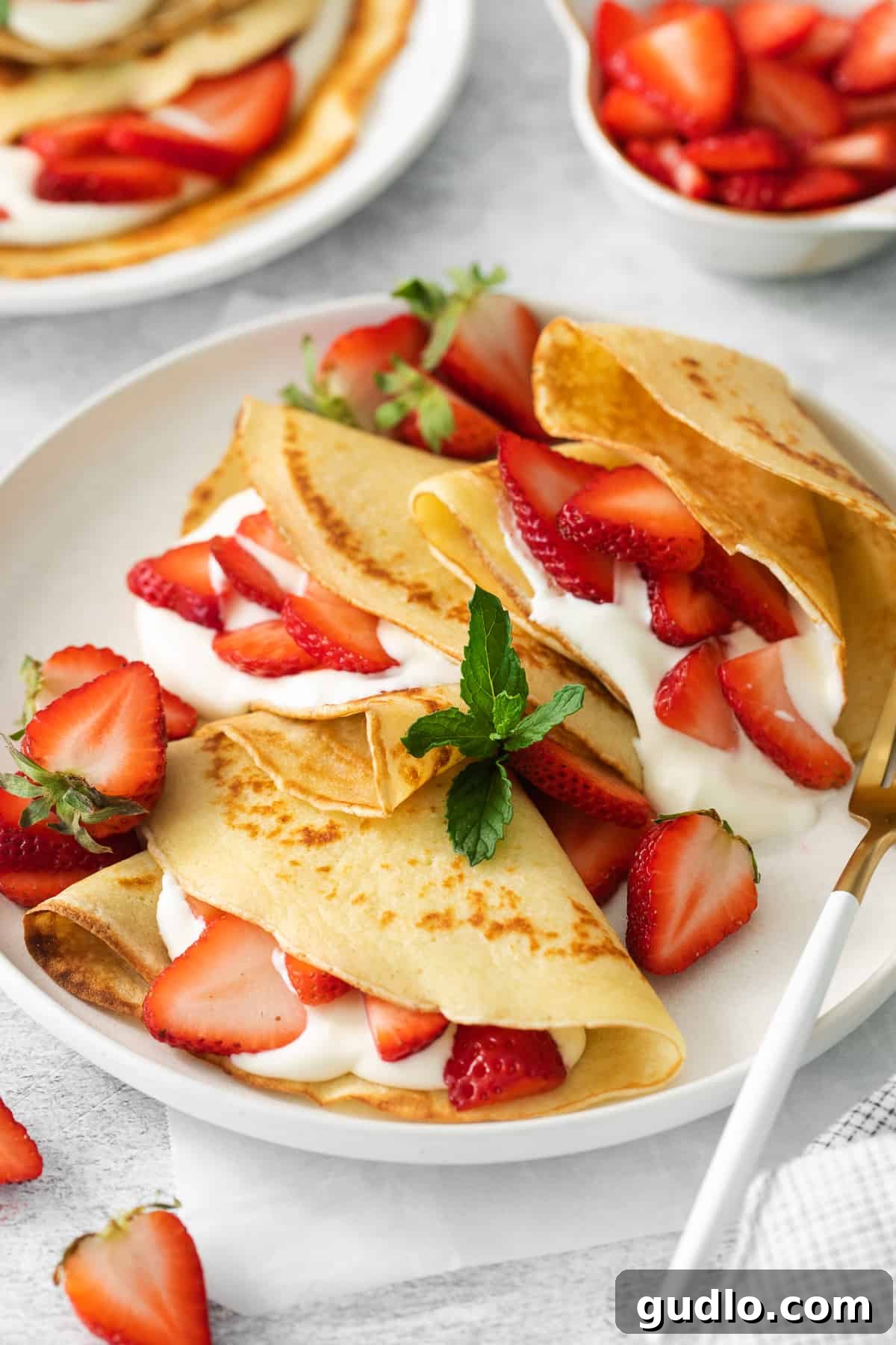 Two strawberry crepes on a plate with a fork, ready to be eaten.
